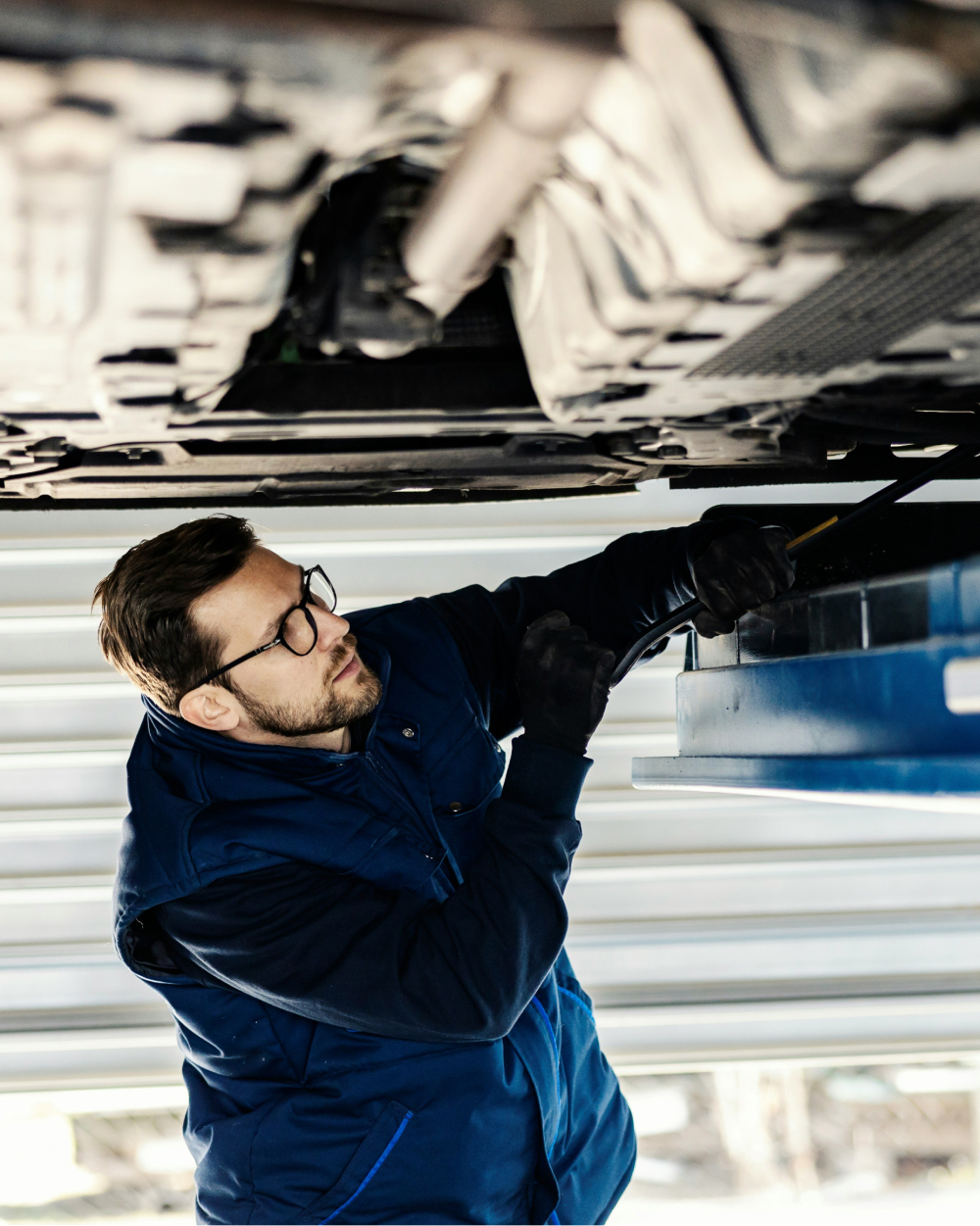 Upper body shot of a man working on the underside of a car.