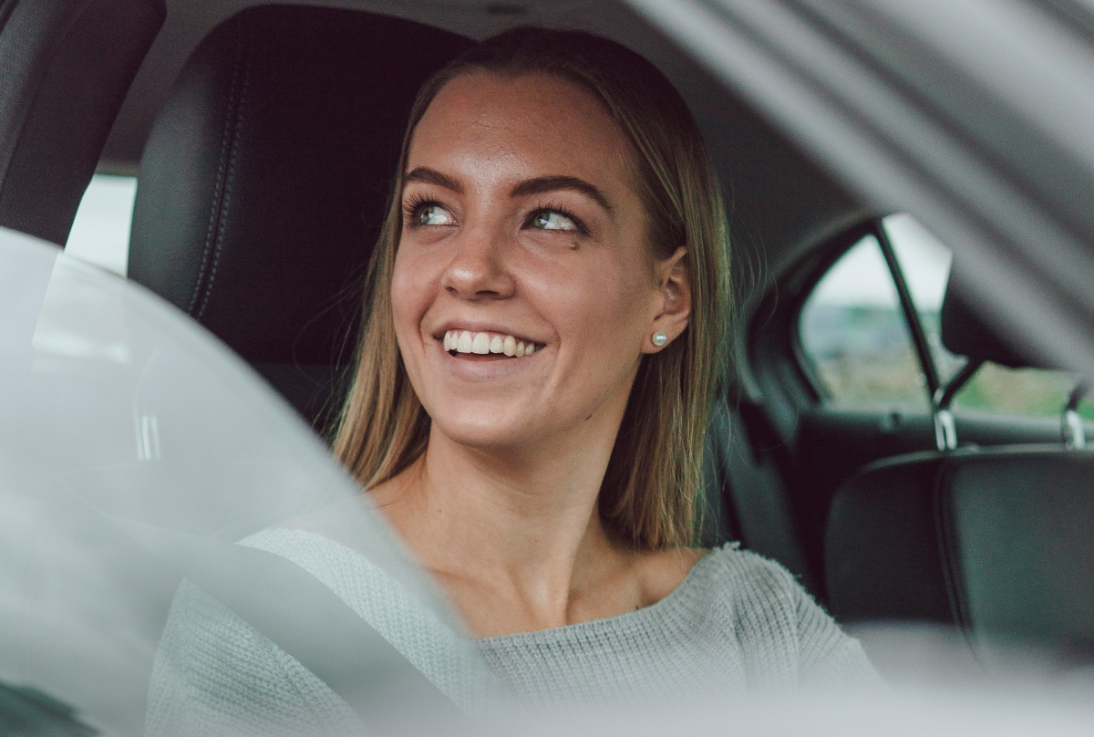 Close-up of a blonde young woman sitting in a car looking out the window while smiling.
