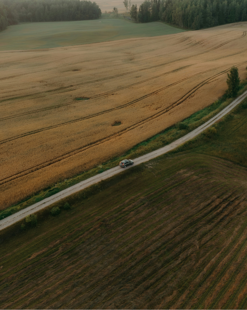 landscape photography of a car driving along a road between two fields