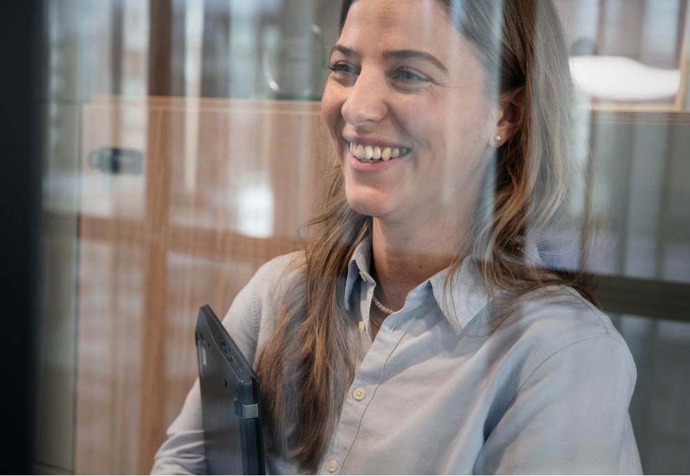 Bild på en kvinna i kontorsmiljö som tittar på något utanför bild medan hon ler.